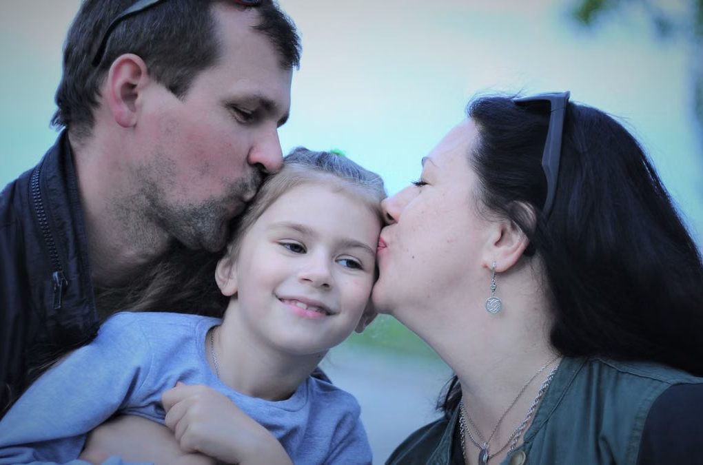 A heartwarming capture of parents showing love to their smiling daughter with gentle kisses.