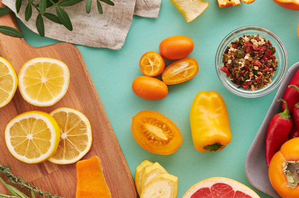 Colorful assortment of sliced fruits and vegetables on teal background, showcasing freshness.