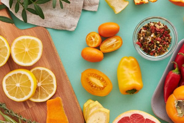Colorful assortment of sliced fruits and vegetables on teal background, showcasing freshness.